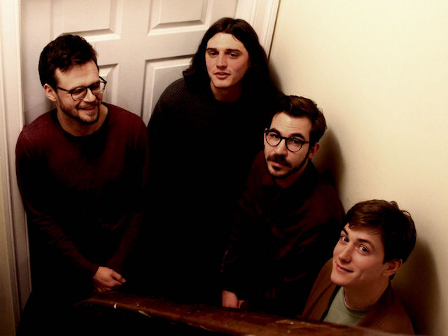 A photo of the band from the top of a residential staircase. They are looking up at the camera.