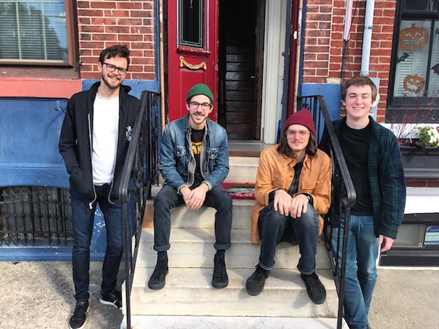 The band sitting on a row home stoop, smiling at the camera.