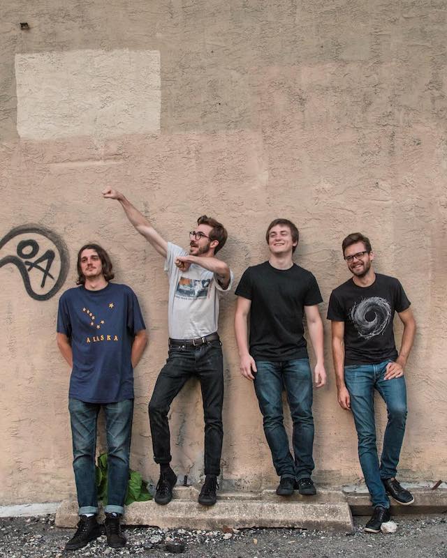 The band lined up along an outdoor wall, looking directly at the camera.